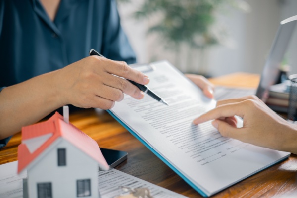 Mains signant sur une tablette à côté d'une maison miniature