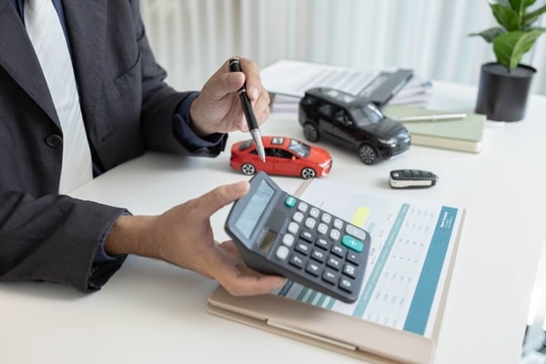 Mains utilisant une calculatrice à côté d'une voiture miniature